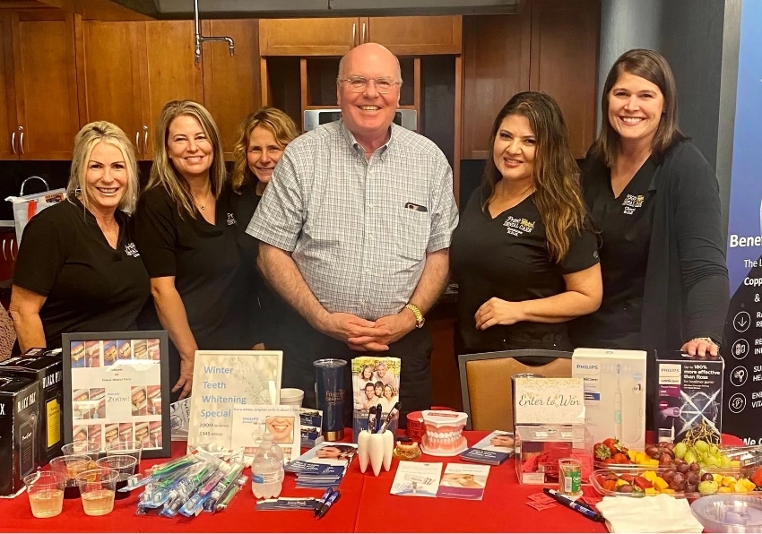Frisco Dental Care team smiling at table with refreshments and oral care supplies