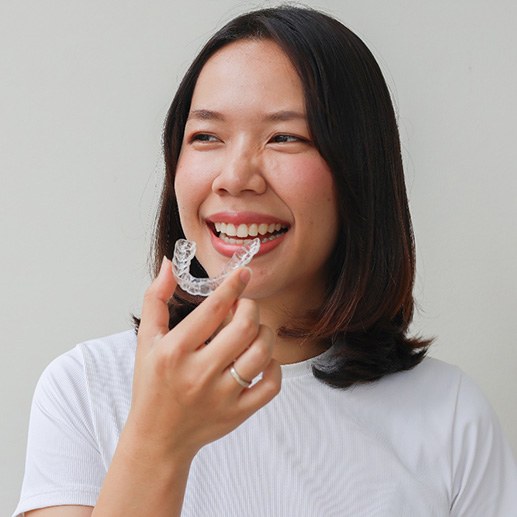 Smiling patient holding clear aligner