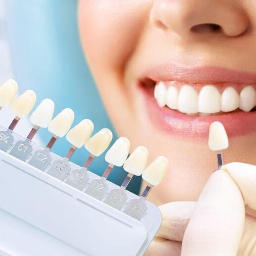 Cosmetic dentist holding a veneer in front of a smiling patient