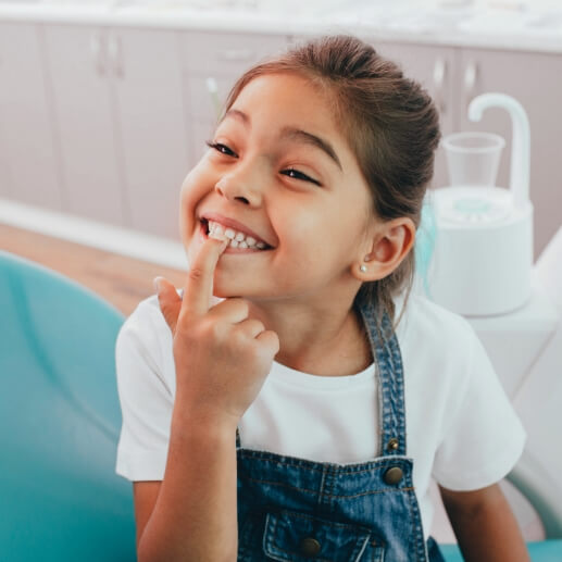 Young girl in dental chair pointing to her smile