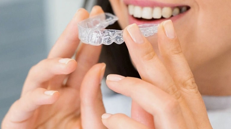 Woman holding Invisalign aligner near her smile