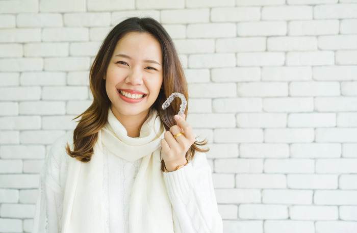 Smiling woman holding an Invisalign clear aligner