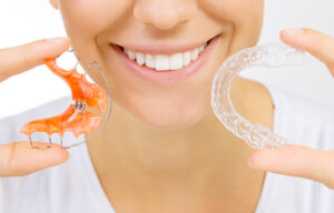 Woman holding clear aligner and retainer. 